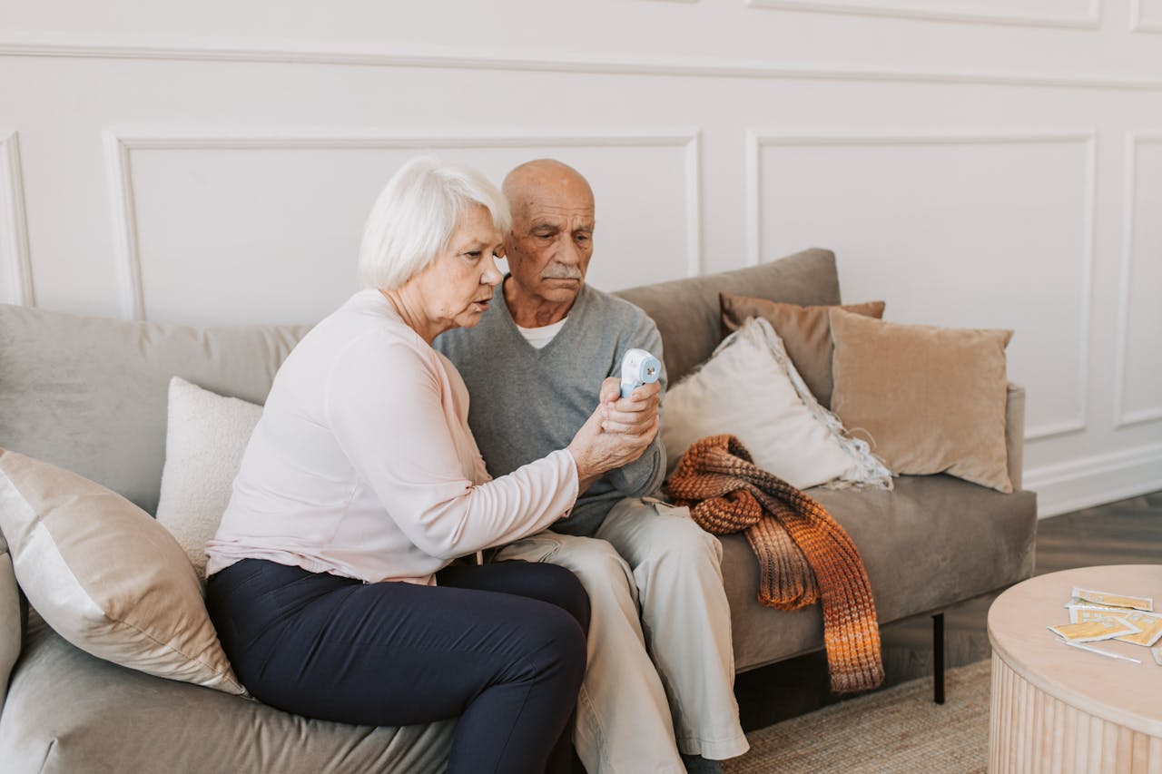 Elderly couple checking temperature with digital thermometer, highlighting health care at home.